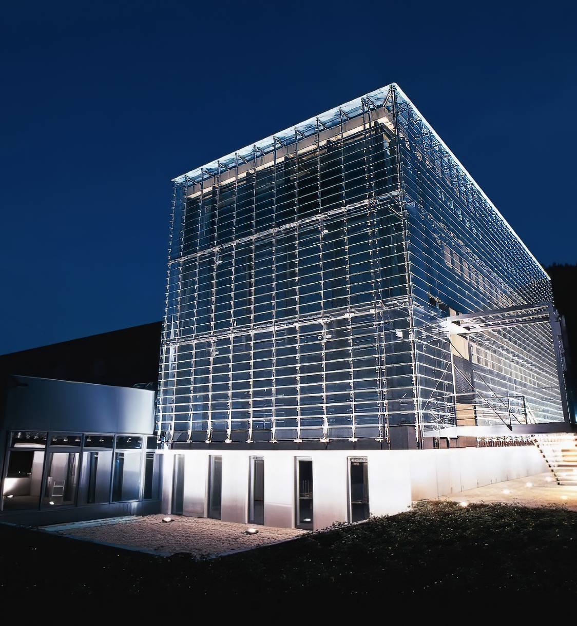Modernes Glasgebäude bei Nacht, beleuchtet.