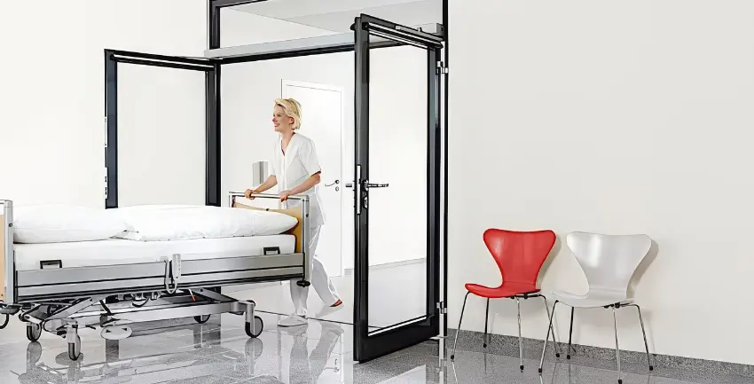 Krankenschwester schiebt Krankenhausbett durch automatisches Türsystem.