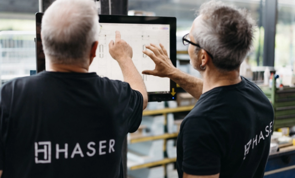 Zwei Ingenieure arbeiten gemeinsam an einem Computerbildschirm und prüfen einen Entwurf. Der Bildschirm zeigt technische Zeichnungen. Das HASER-Logo ist sichtbar.