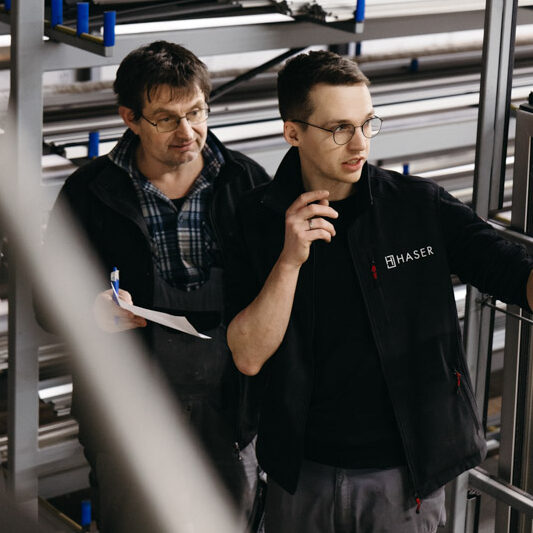 Zwei Männer arbeiten in einer Fabrik an einem Projekt. Ein Mann hält Papierkram in der Hand.