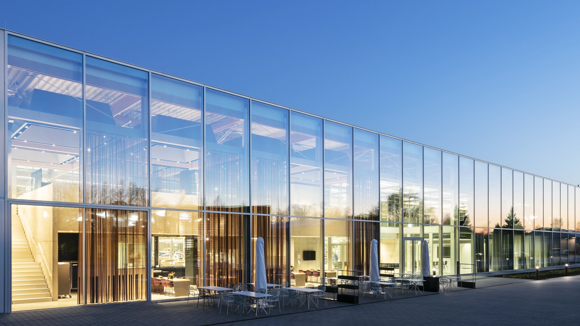Modernes Glasgebäude in der Abenddämmerung mit Sitzbereich im Freien.