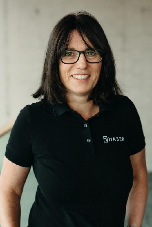 http://Porträt%20einer%20Frau%20mit%20schwarzem%20Haser-Poloshirt%20und%20Brille.