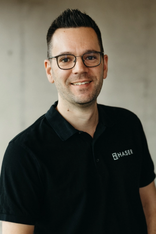 http://Porträt%20eines%20lächelnden%20Haser-Mitarbeiters%20in%20einem%20schwarzen%20Poloshirt.