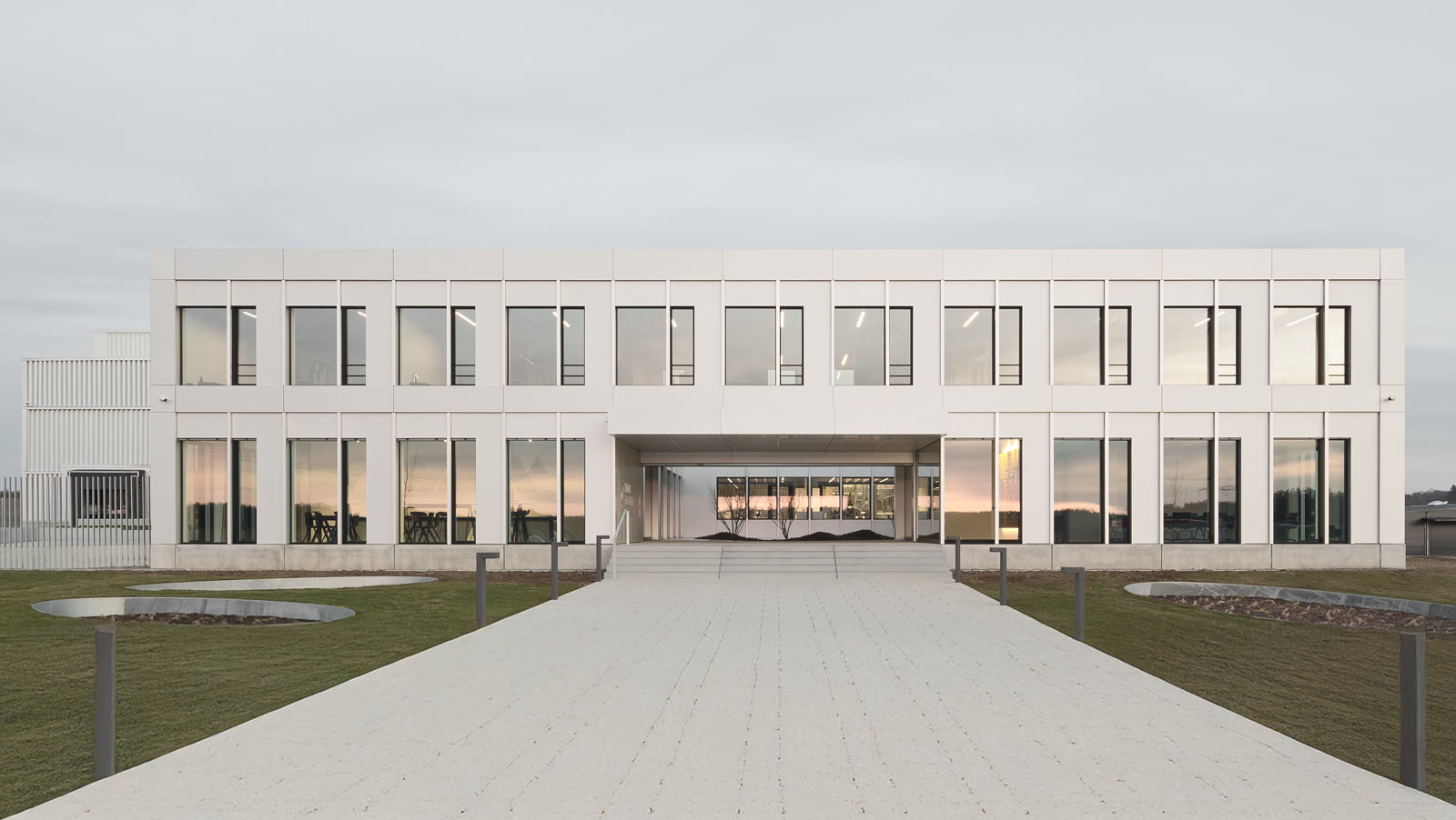Modernes weißes Bürogebäude mit großen Fenstern, die den Sonnenuntergang reflektieren.